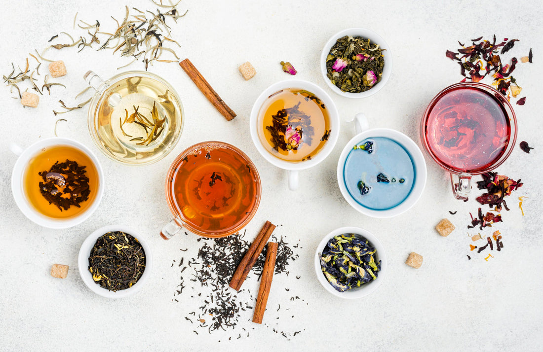 Various cups of colorful herbal and loose leaf teas with cinnamon sticks and sugar cubes on white background