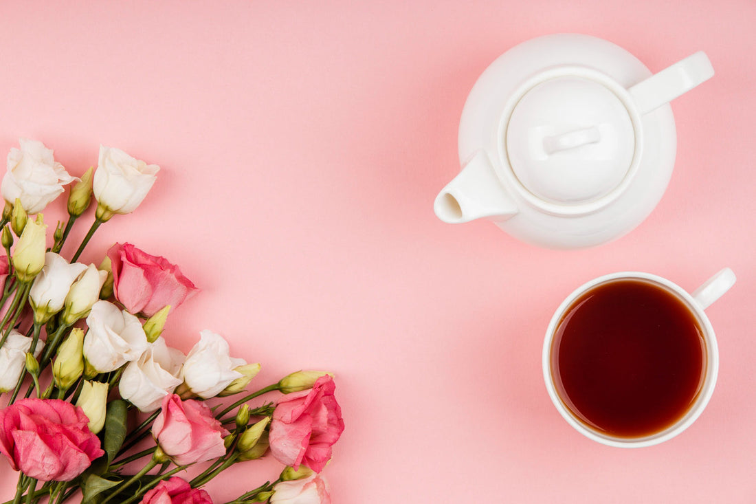 White teapot and cup of tea with pink and white flowers on pink background