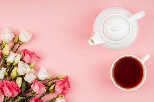 White teapot and cup of tea with pink and white flowers on pink background