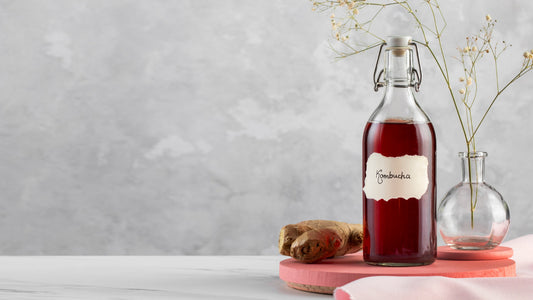 Glass bottle of red kombucha with ginger root and small flowers on pink and white marble surface