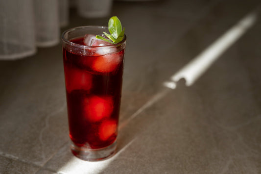 Tall glass of red iced beverage with mint garnish on stone surface in sunlight