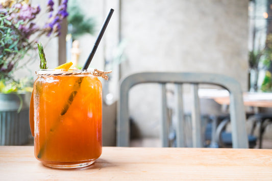 Glass jar with orange iced cocktail garnished with rosemary and lemon on wooden table