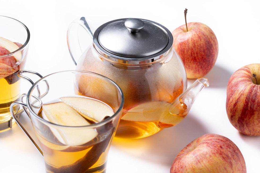 Glass teapot and cups with apple cinnamon tea and fresh red apples on white