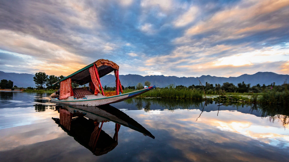 Traditional wooden boat with colorful canopy floating on calm lake at sunset with mountains and reflection