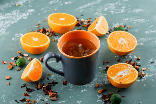 Black mug with orange interior filled with tea surrounded by halved fresh oranges and dried fruit pieces