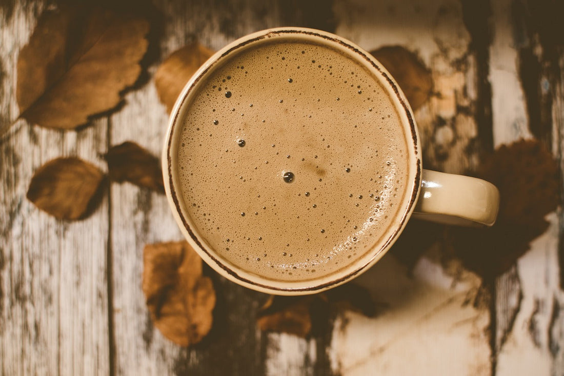 Top view of a creamy coffee in a beige mug on rustic wood table with dried autumn leaves
