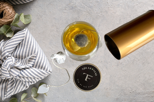Top view of a glass cup with tea bag steeping, striped cloth bundle, jar lid, and golden cylindrical container on concrete surface